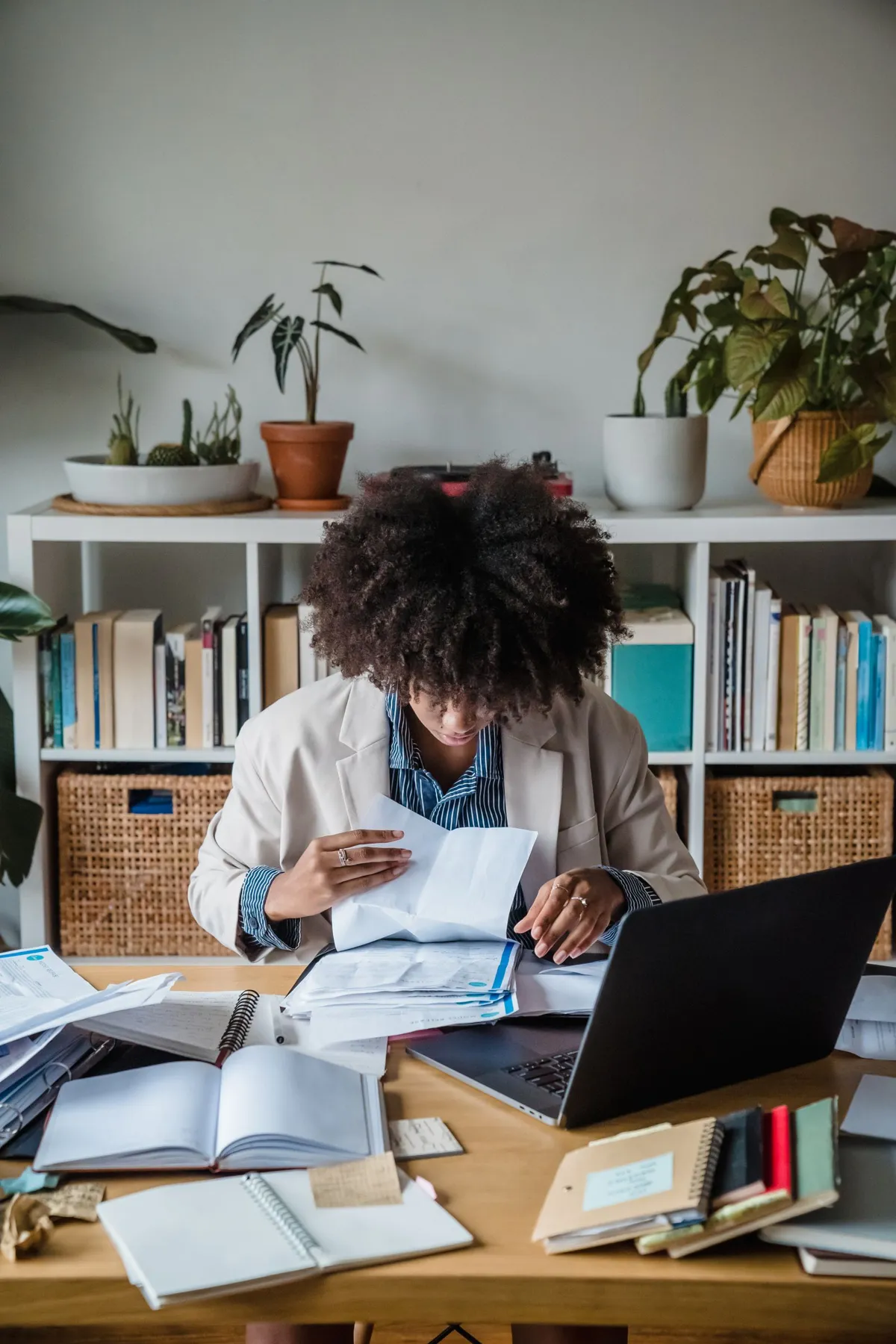 A researcher at a desk sorting printed interview notes and reports beside a laptop
